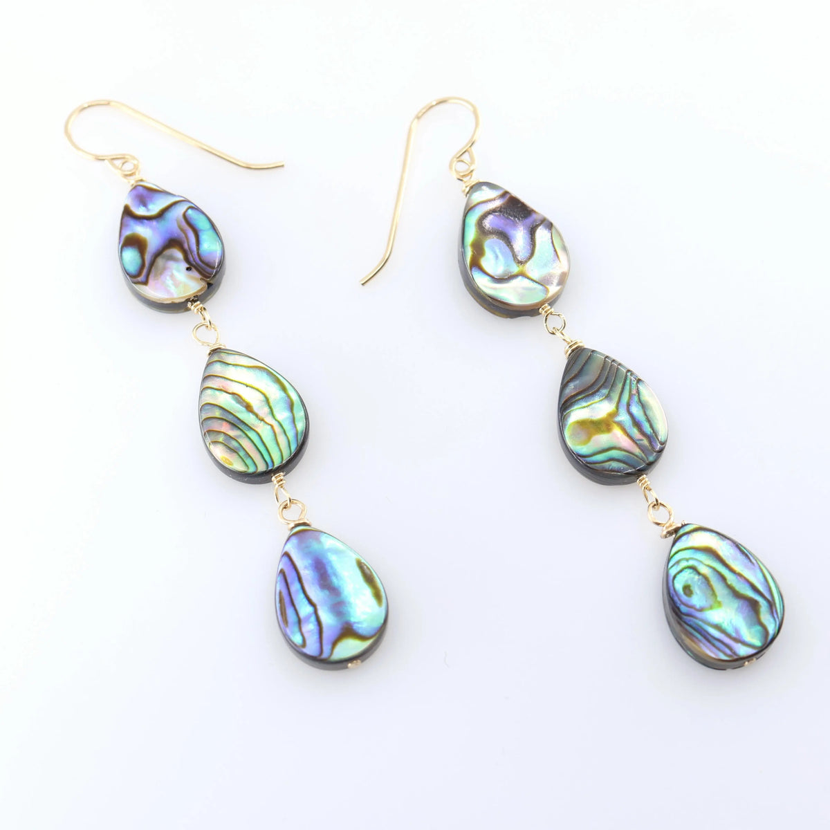 A pair of dangle earrings with three teardrop-shaped abalone shell pendants, showcasing a shimmering iridescent green, blue, and purple coloration, set against a clean white background.