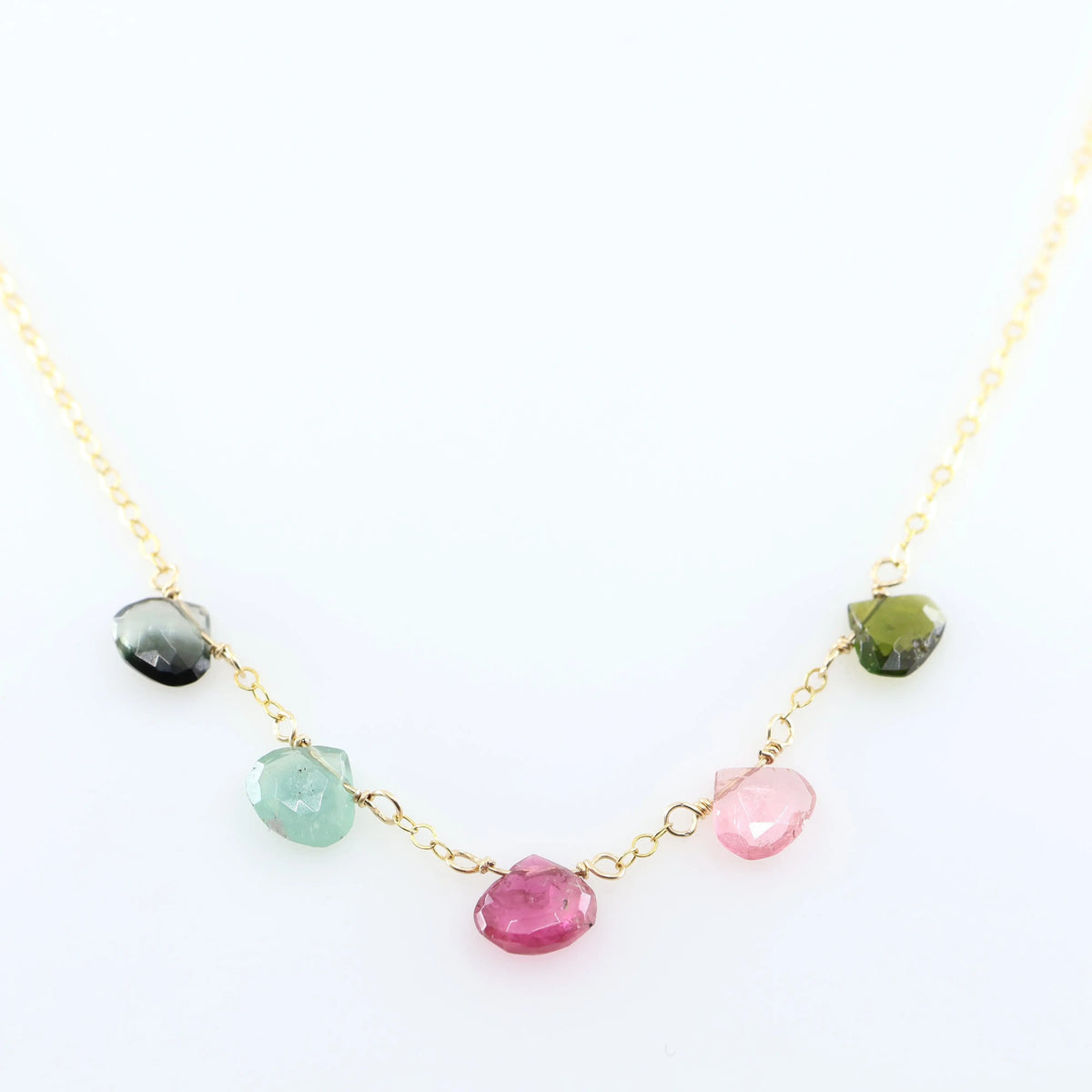 A delicate gold chain necklace featuring five small, hand-cut Watermelon Tourmaline gemstone teardrops; displayed on a clean white background.