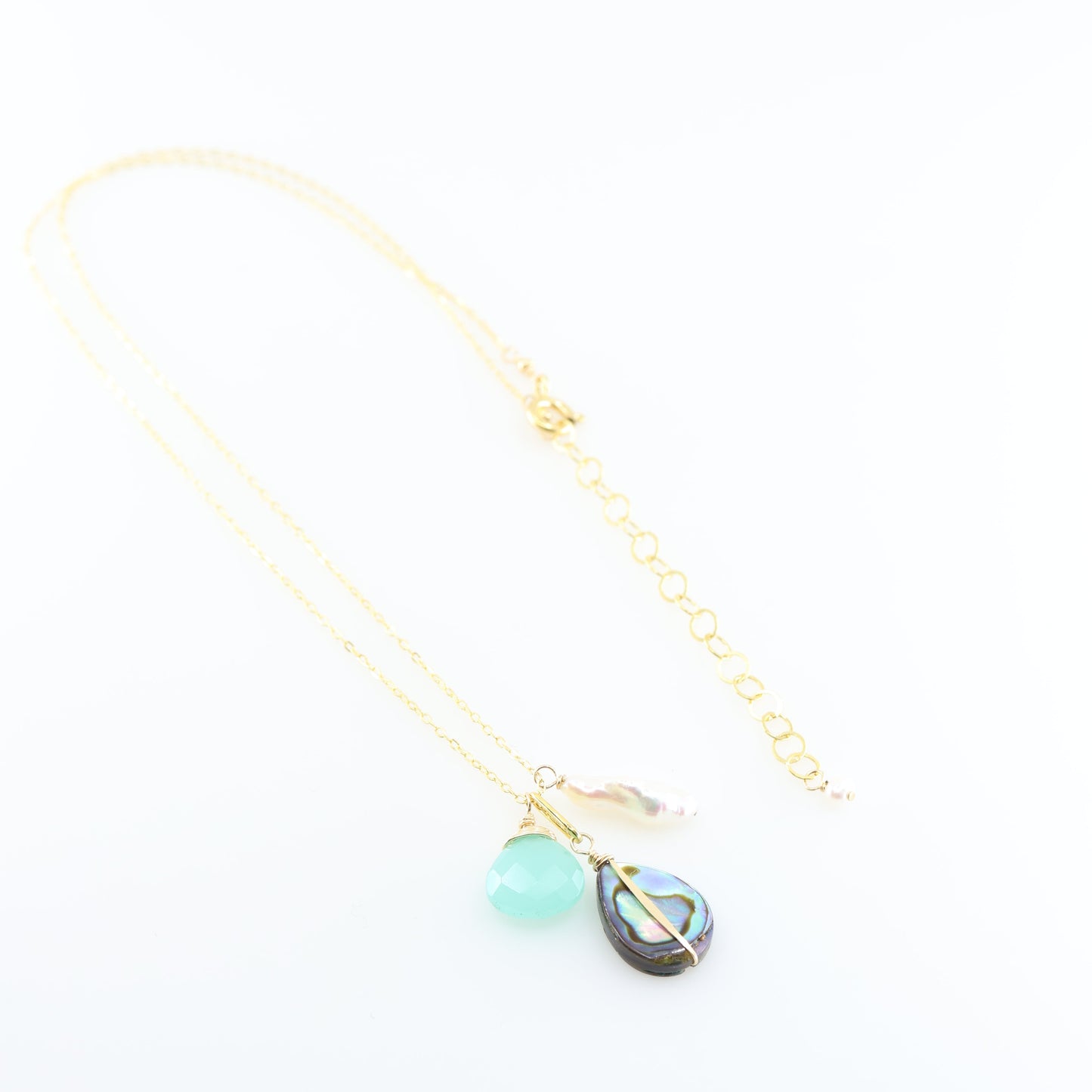 A gold chain necklace featuring triple pendant design: a faceted Dark Aqua Chalcedony gemstone, a teardrop-shaped iridescent abalone shell, and a small Biwa pearl, set against a clean white background.