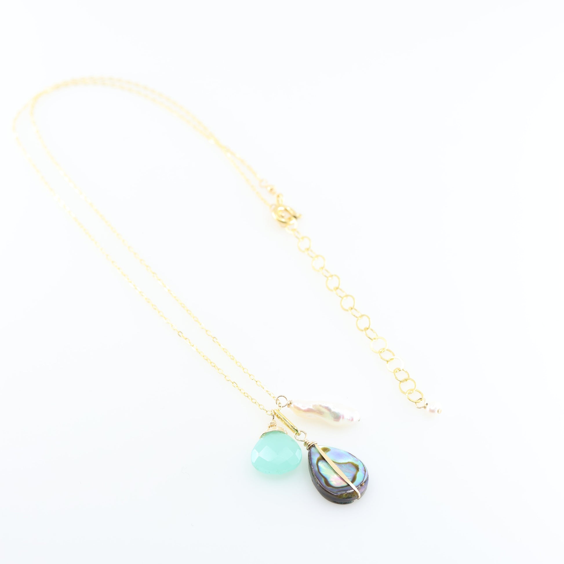 A gold chain necklace featuring triple pendant design: a faceted Dark Aqua Chalcedony gemstone, a teardrop-shaped iridescent abalone shell, and a small Biwa pearl, set against a clean white background.