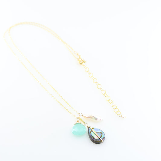 A gold chain necklace featuring triple pendant design: a faceted Dark Aqua Chalcedony gemstone, a teardrop-shaped iridescent abalone shell, and a small Biwa pearl, set against a clean white background.