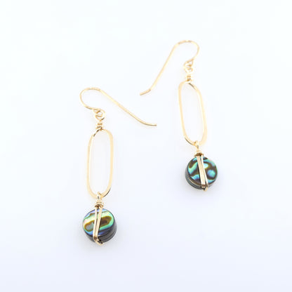 A pair of gold drop earrings with elongated oval hand forged pendant and round iridescent Abalone featuring green, blue, and black swirls, displayed on a clean white background.