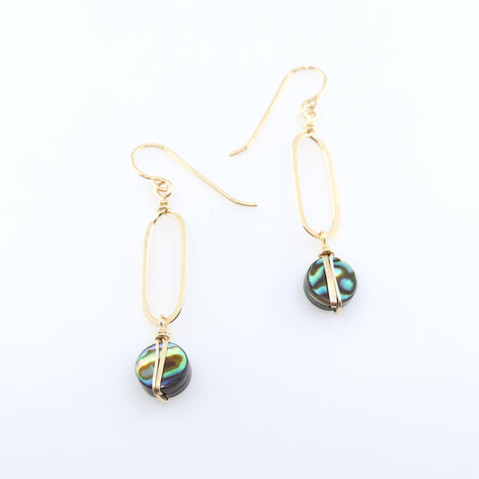 A pair of gold drop earrings with elongated oval hand forged pendant and round iridescent Abalone featuring green, blue, and black swirls, displayed on a clean white background.