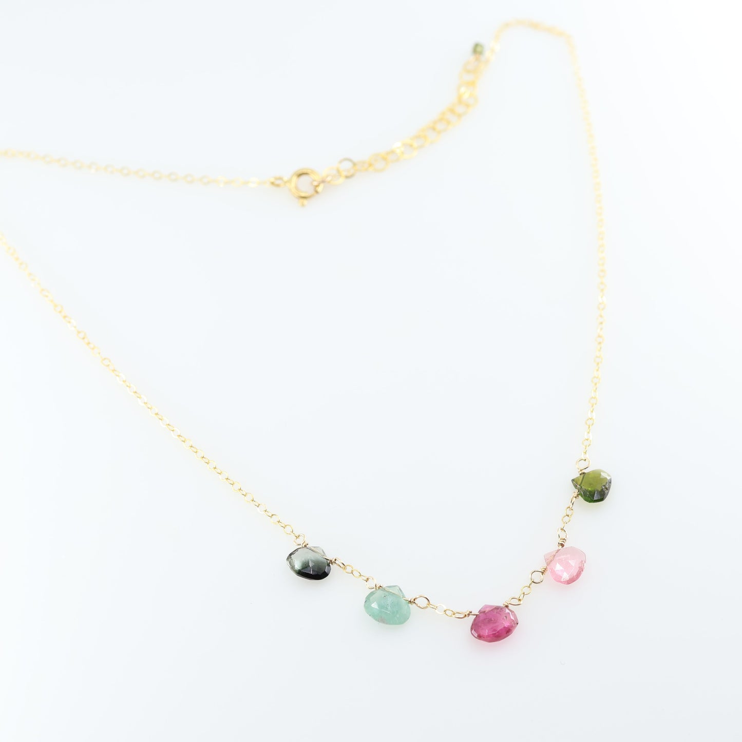 A delicate gold chain necklace featuring five small, hand-cut Watermelon Tourmaline gemstone teardrops; displayed on a clean white background.