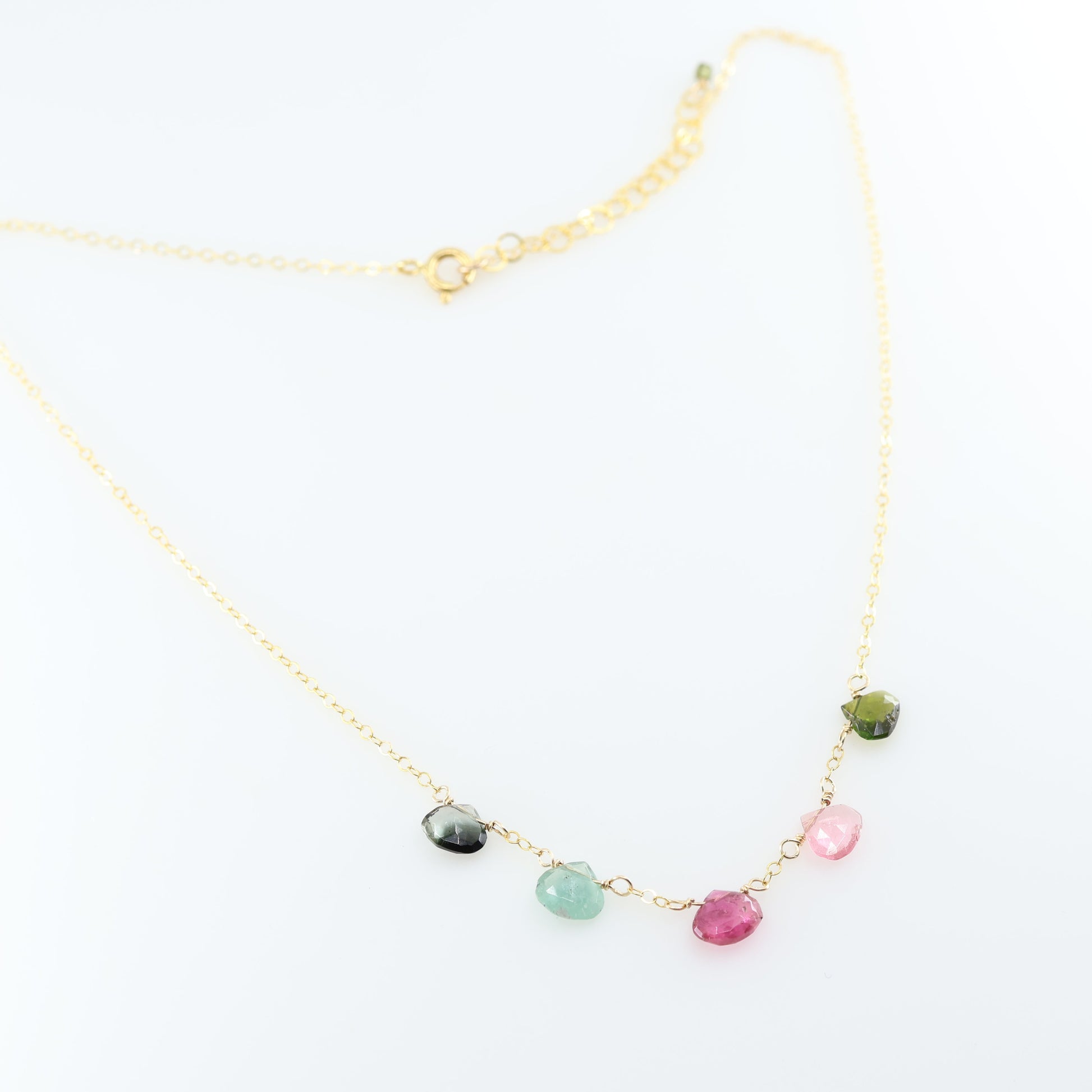 A delicate gold chain necklace featuring five small, hand-cut Watermelon Tourmaline gemstone teardrops; displayed on a clean white background.