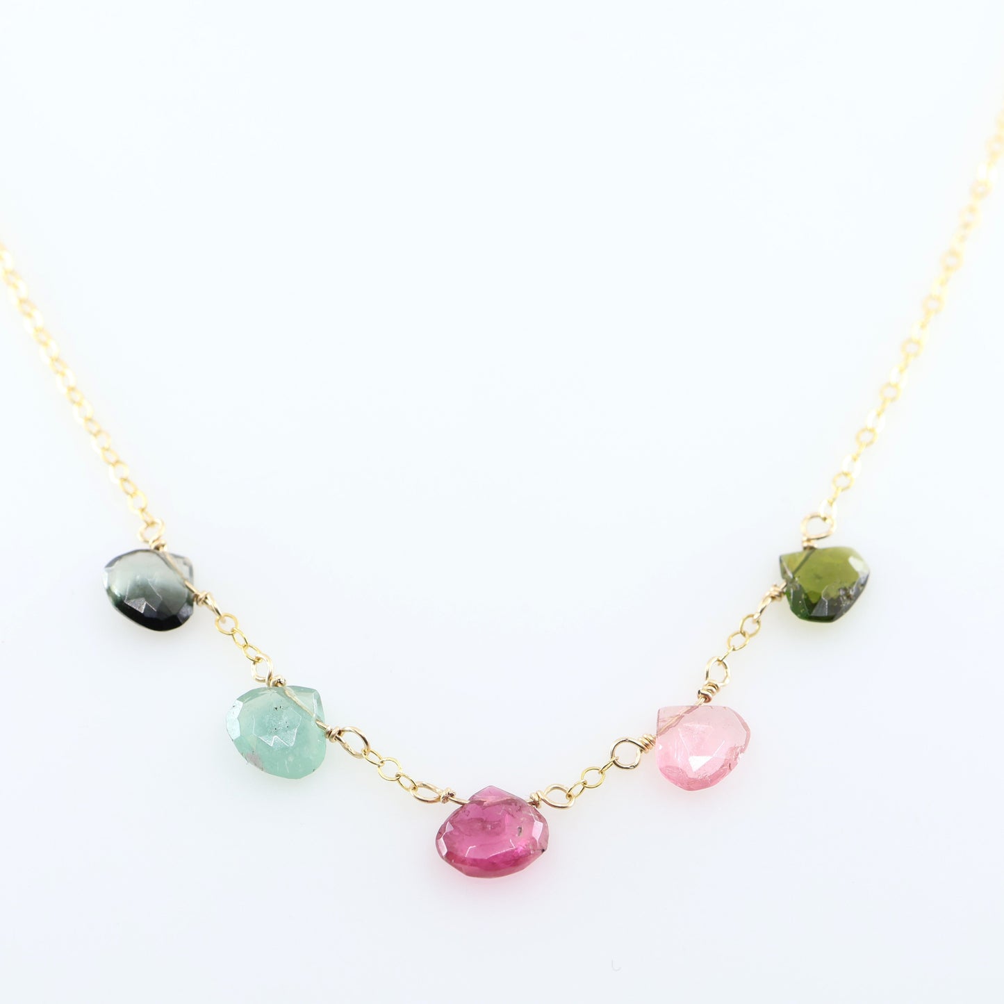 A delicate gold chain necklace featuring five small, hand-cut Watermelon Tourmaline gemstone teardrops; displayed on a clean white background.