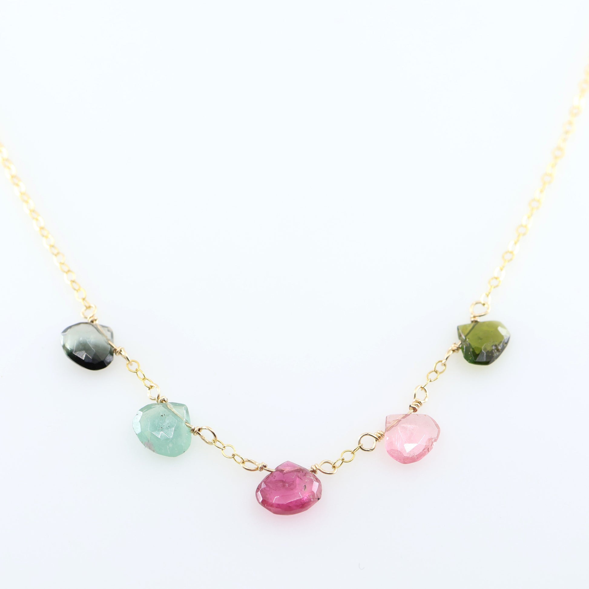 A delicate gold chain necklace featuring five small, hand-cut Watermelon Tourmaline gemstone teardrops; displayed on a clean white background.