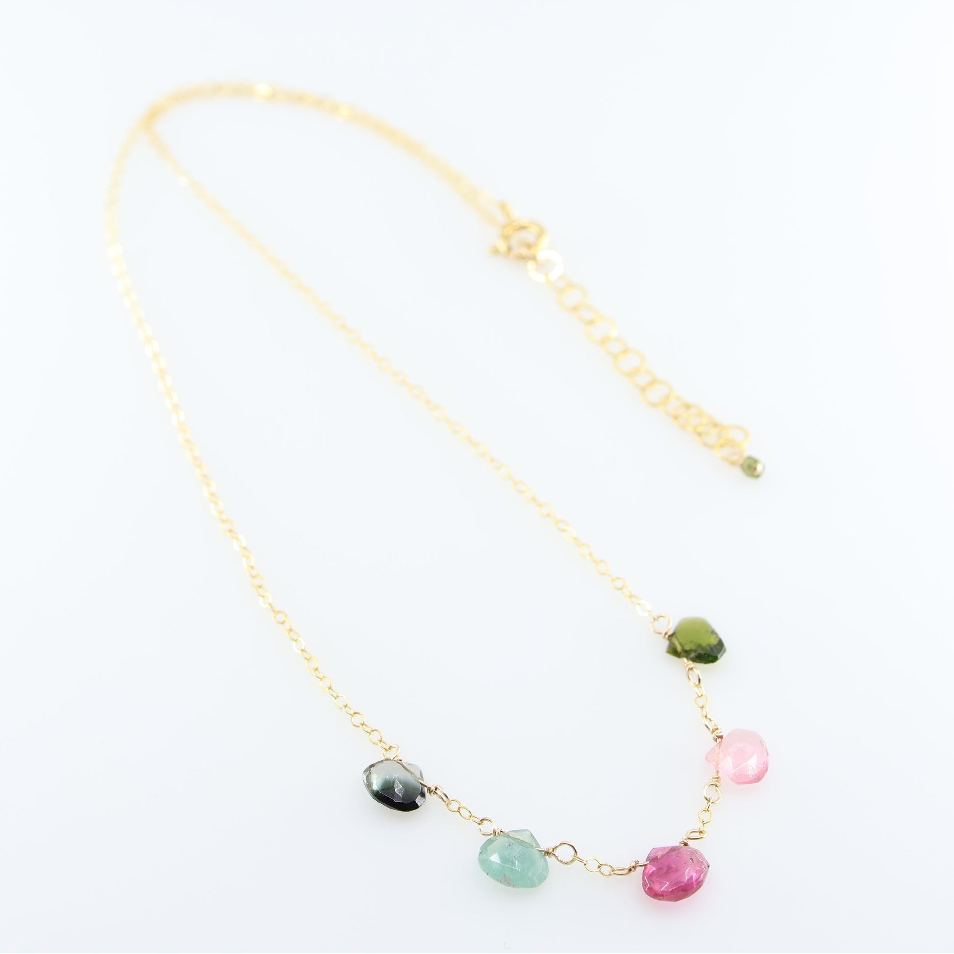 A delicate gold chain necklace featuring five small, hand-cut Watermelon Tourmaline gemstone teardrops; displayed on a clean white background.