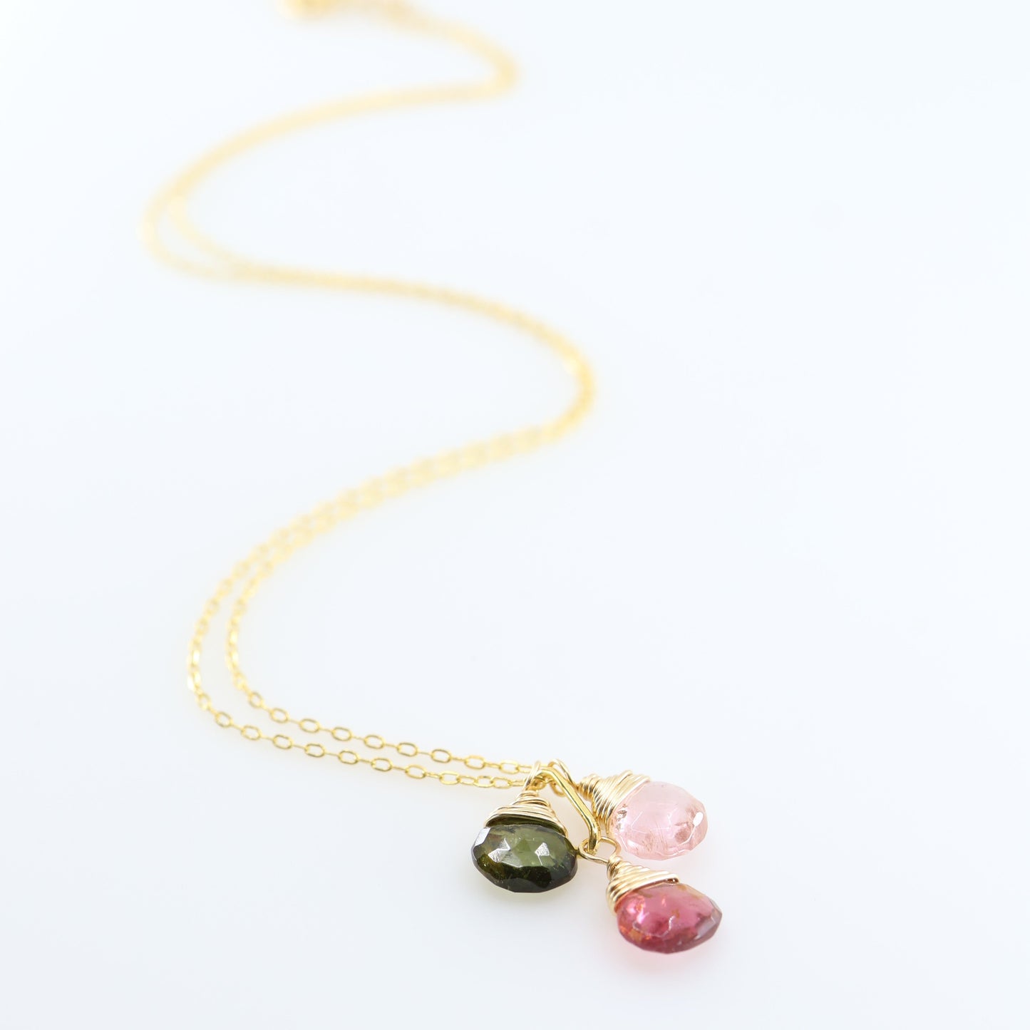 A delicate gold chain necklace with three small, colorful gemstone pendants in gold settings, displayed on a clean white background.