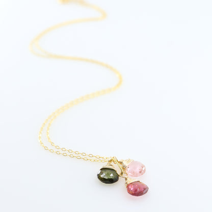 A delicate gold chain necklace with three small, colorful gemstone pendants in gold settings, displayed on a clean white background.